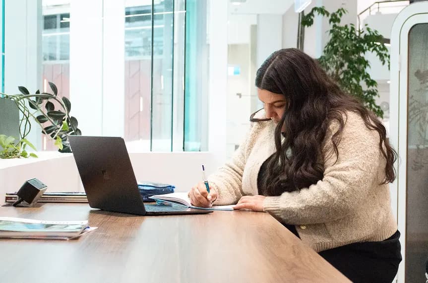 A tender professional writing beside her laptop